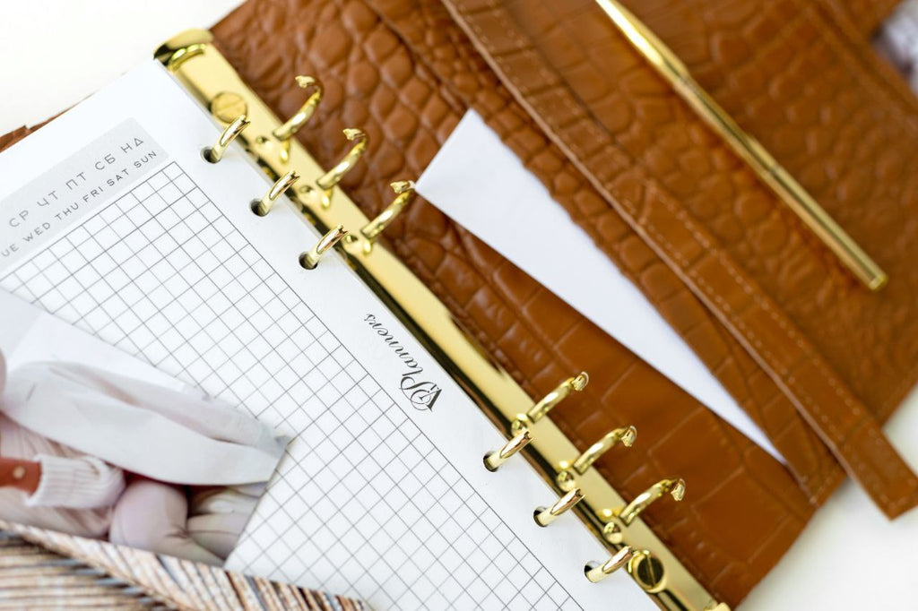 Close-up of a rare brown leather A5 notebook cover with gold binder rings and grid paper inside.