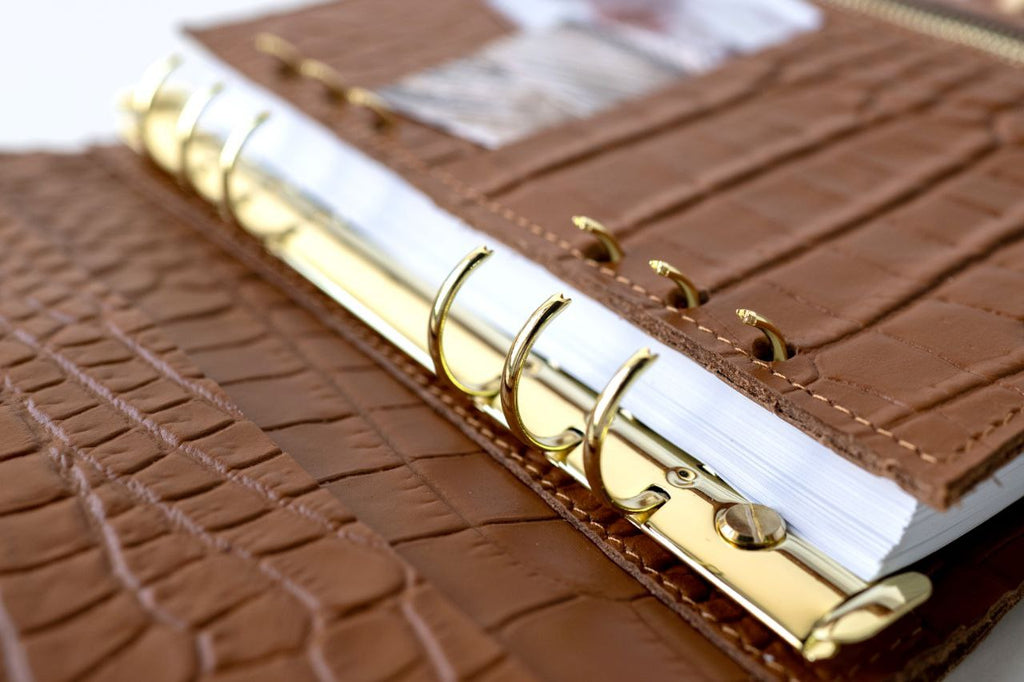 Close-up of a rare brown leather A5 notebook cover with gold binder rings and pages.