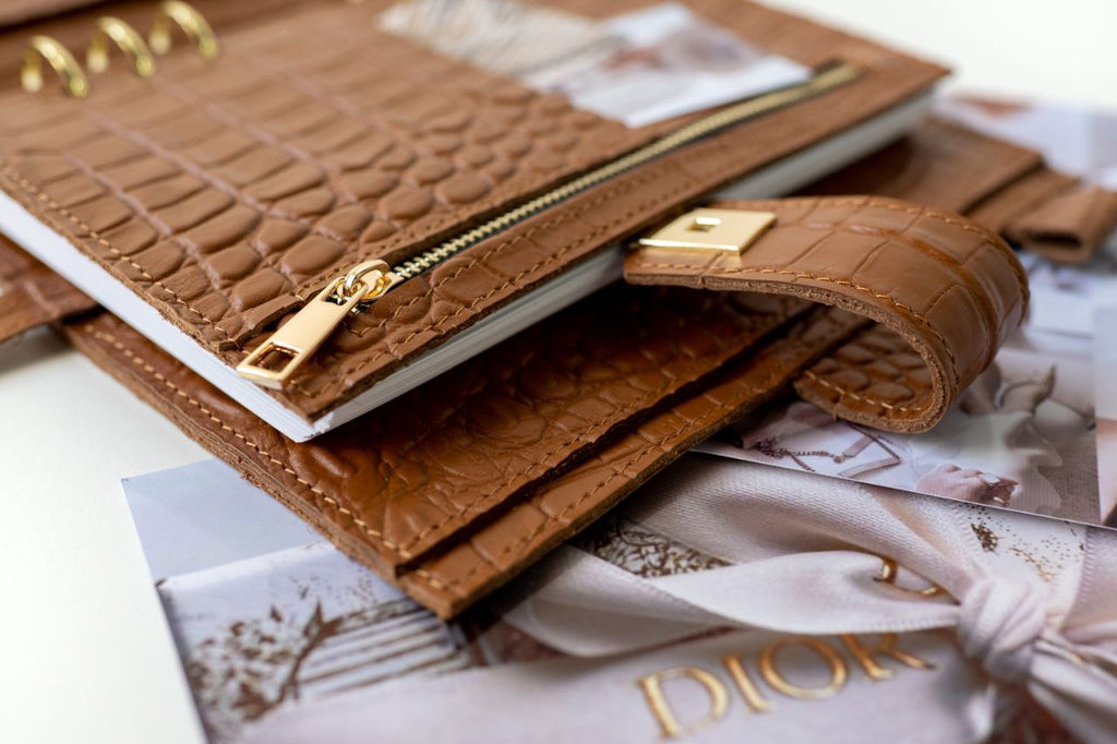 Rare brown leather A5 notebook cover with golden zipper and binder rings, placed on fashion magazines.