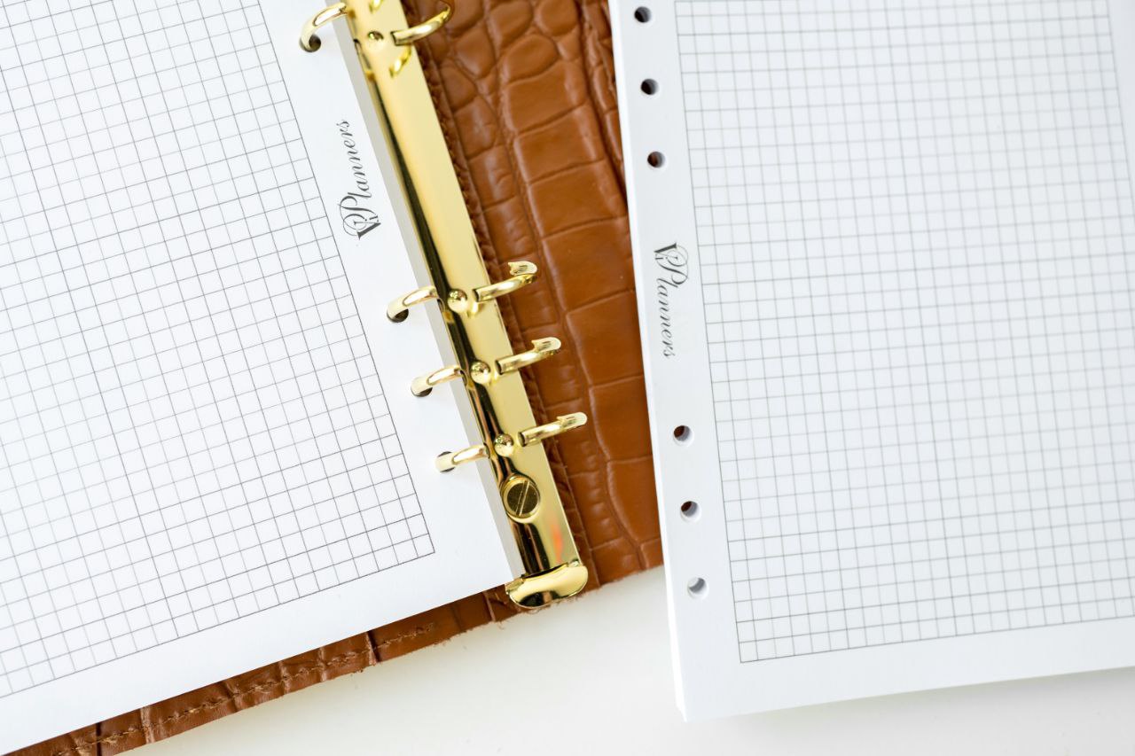 Close-up of brown leather notebook cover with gold binder rings and graph paper inside.